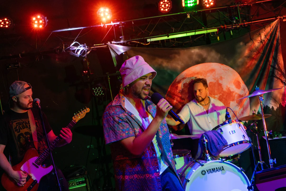 Guitarist, vocalist and drummer mid-song under red stage lights at The Wolf